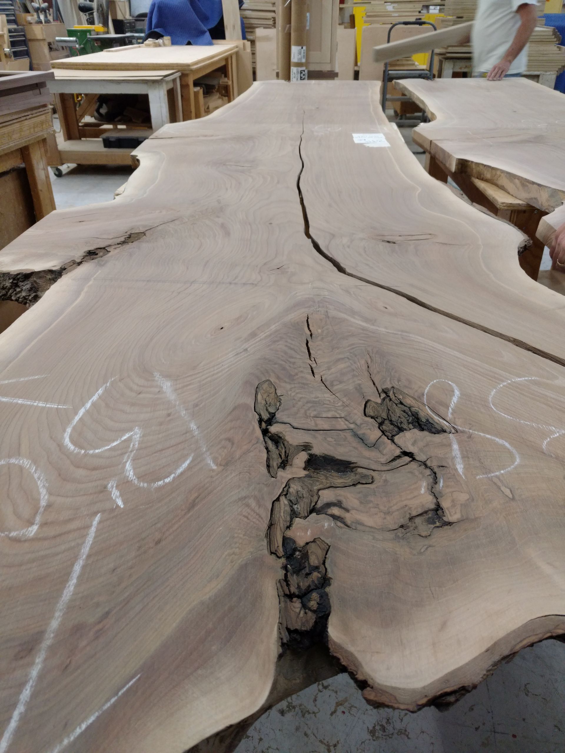 Large, unfinished wood slab with natural edges and a dark, cracked pattern. In a workshop setting, showing the potential for a table.