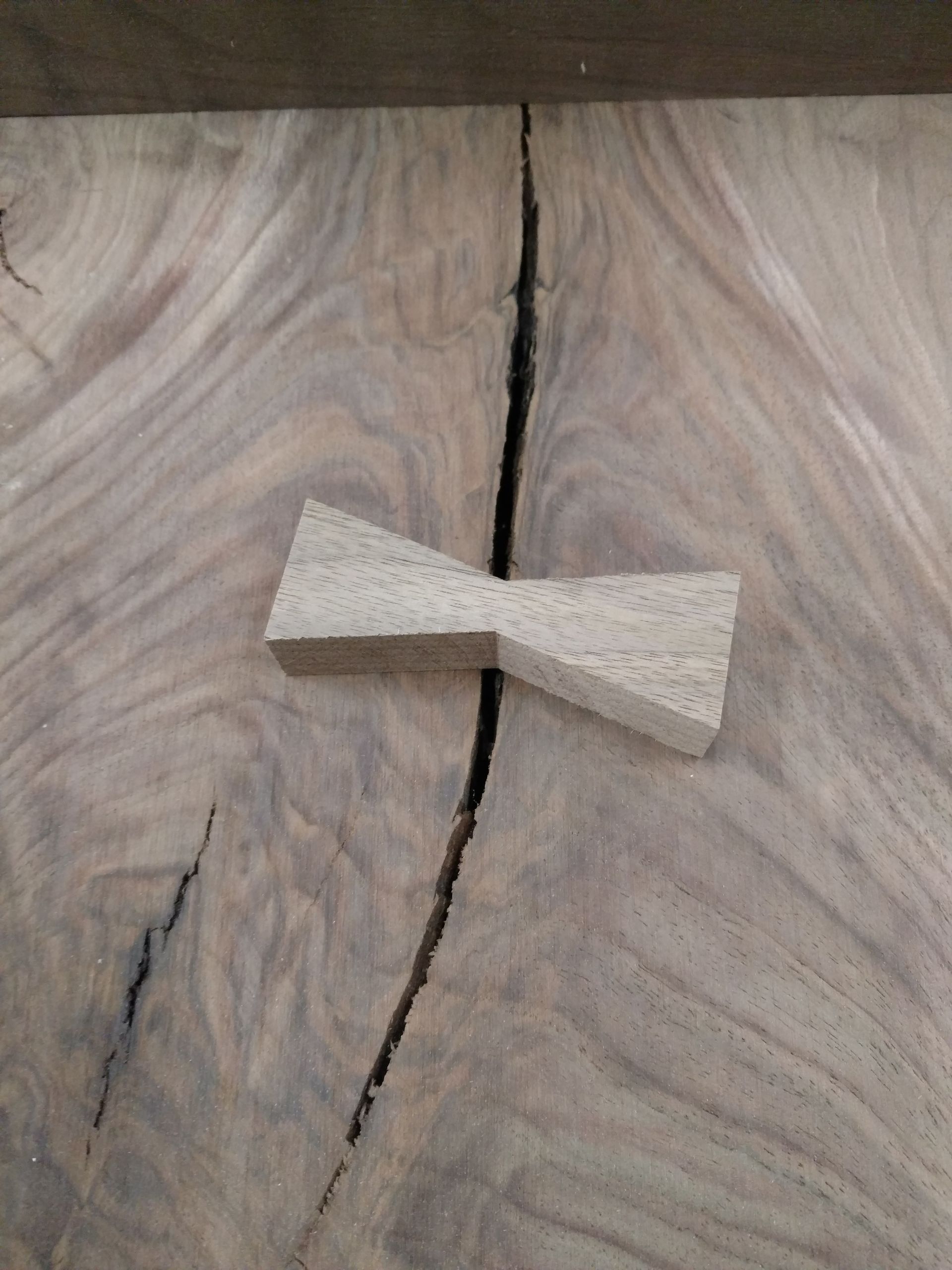 A butterfly-shaped wood joint (bow tie) inlaid across a crack in a large, patterned wooden surface.