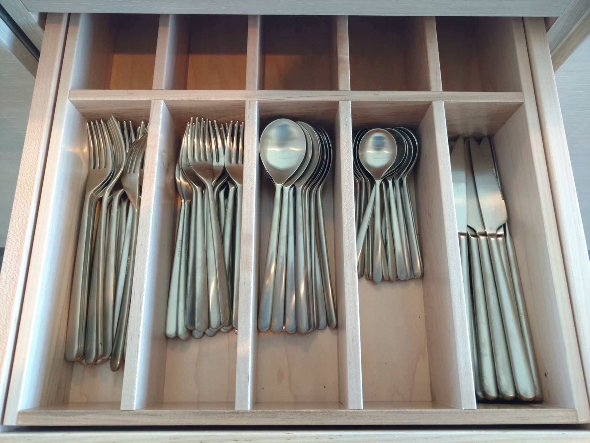 A neatly organized drawer holding silverware; forks, spoons, and knives are separated in wooden compartments.
