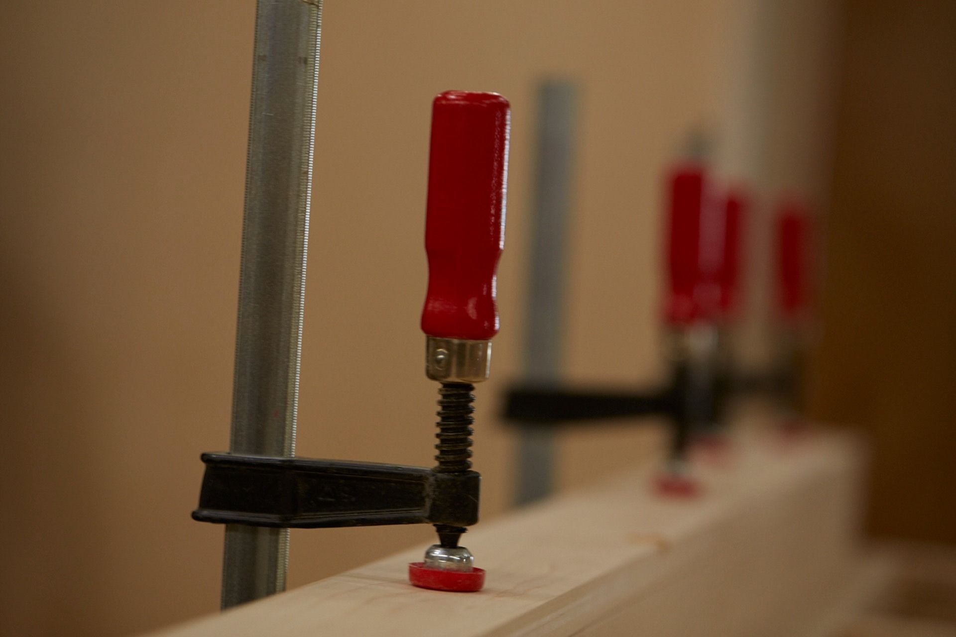 Wooden planks clamped together using four clamps with red handles in a carpentry setting.