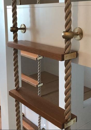 A rope ladder with wooden steps and brass hardware is mounted against a white wall. Another shelf is visible behind the ladder.