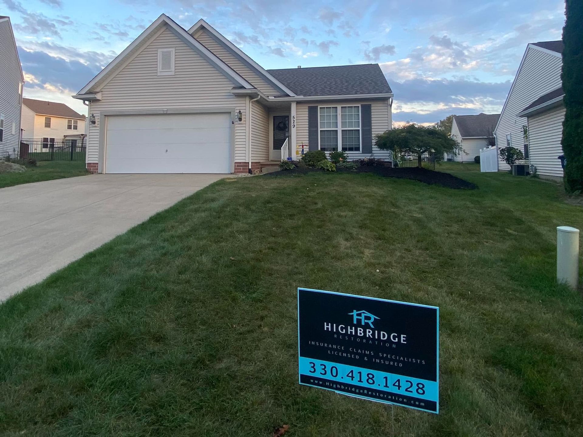 Suburban home with a sign for Highbridge Real Estate on a grassy lawn. Blue sky.