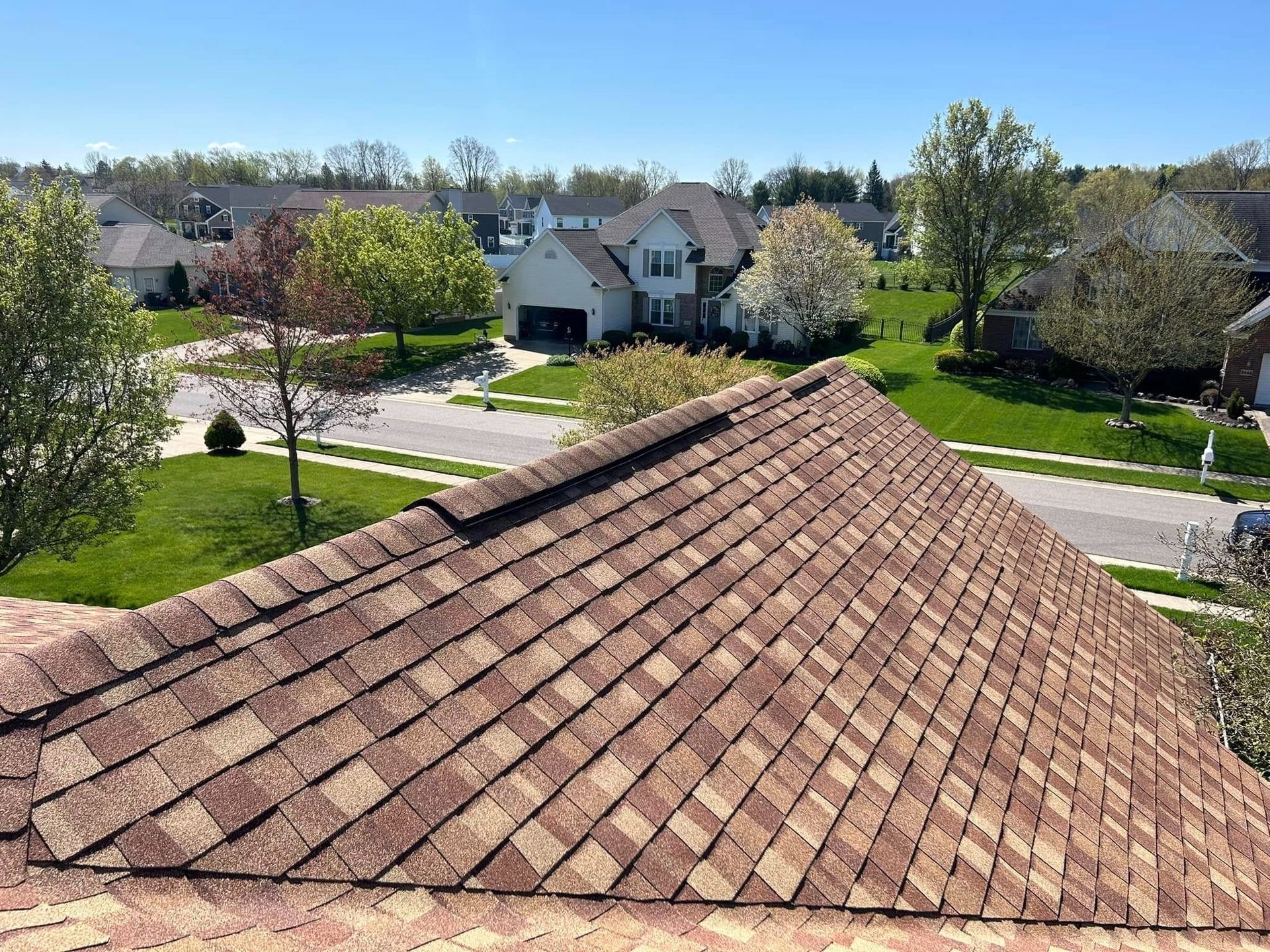 Brown shingle roof with houses and a street in a suburban neighborhood on a sunny day.