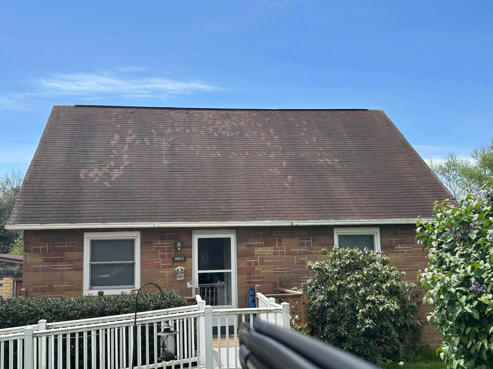 Brick house with a weathered brown roof under a blue sky. White railing in the foreground.