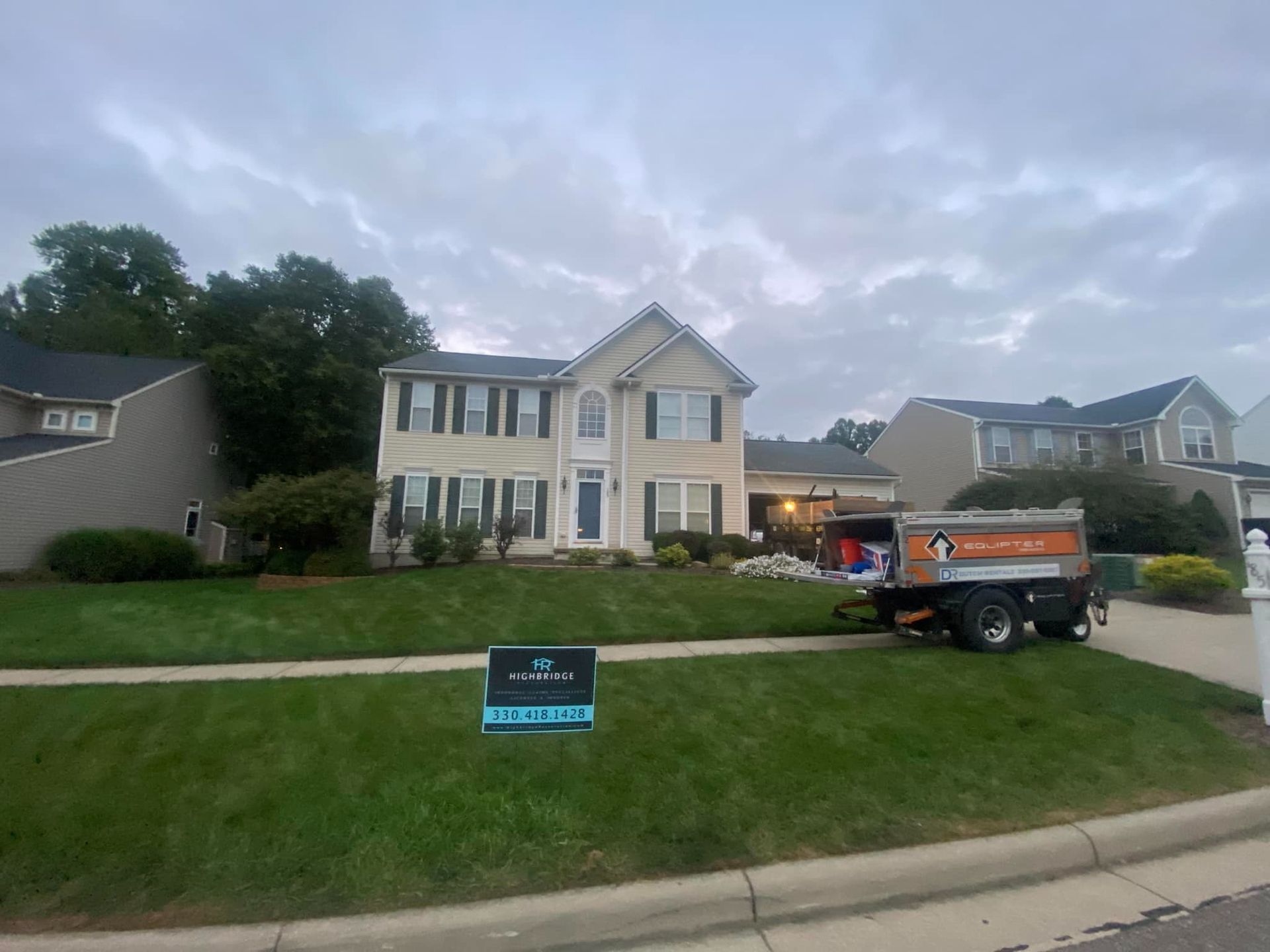 House with a dump truck in front, lawn sign, overcast sky.