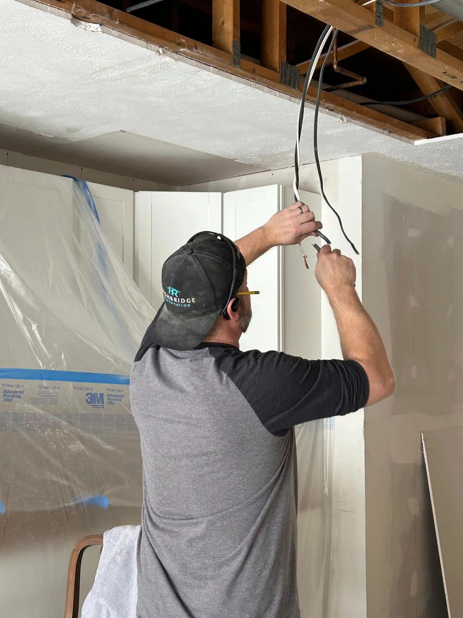 Man working on electrical wires in a ceiling, indoors.