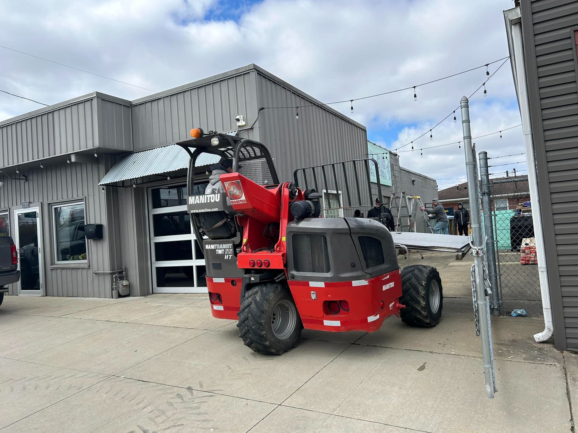 Red telehandler parked near a gray building, outside on a cloudy day.