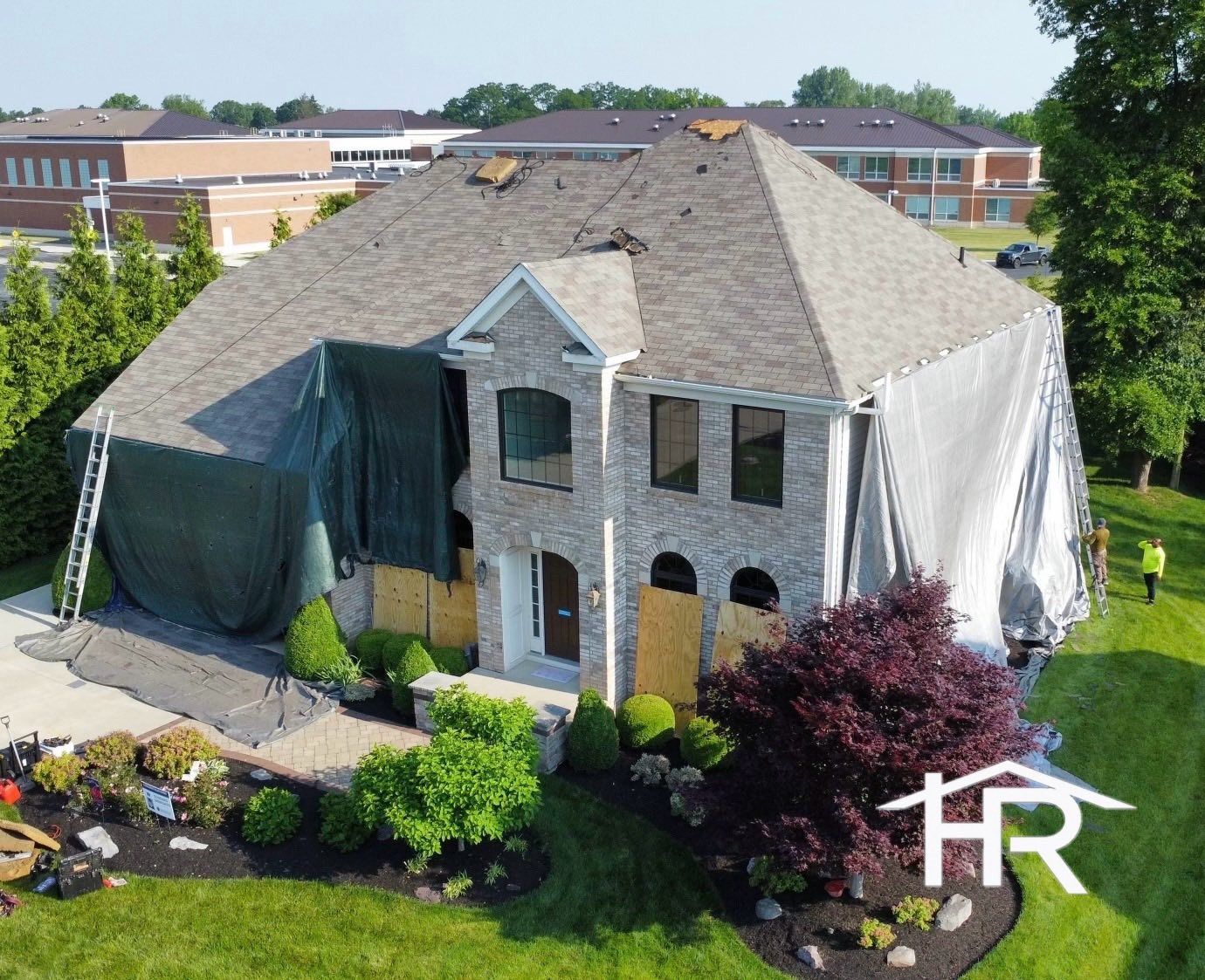 House with roof damage, covered in tarps; construction site. Green and white tarps cover the building.