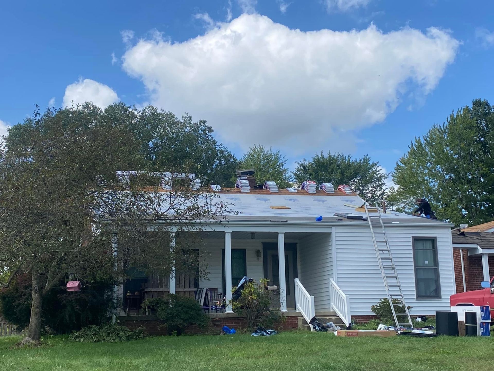 Roofers working on a house with white siding and a porch under a cloudy sky.