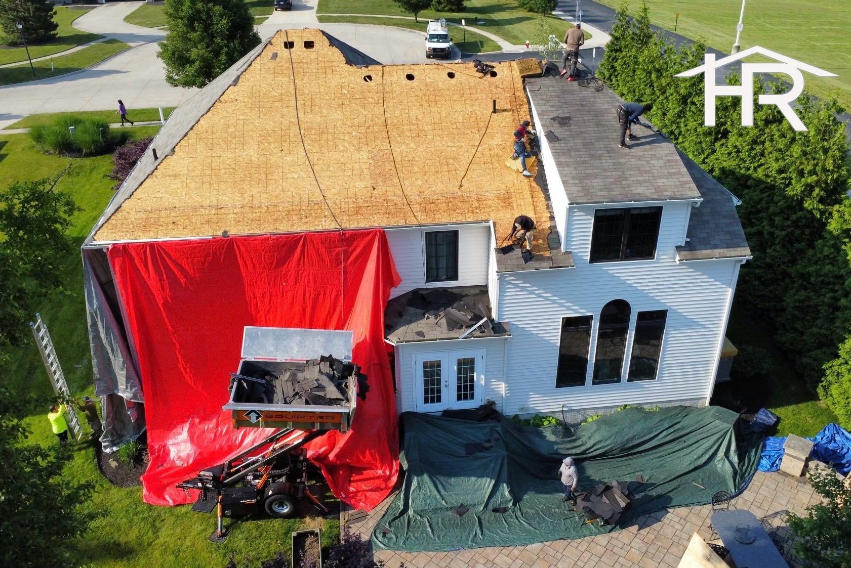House roof being replaced; debris chute; red tarp; workers on the roof.