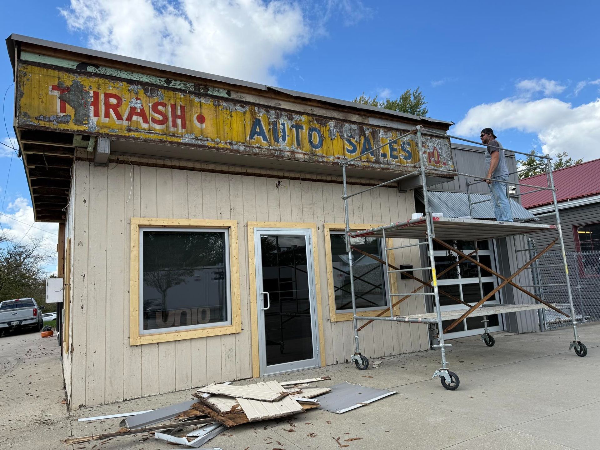 Auto sales building undergoing renovation. A person works on scaffolding. Weathered sign reads 