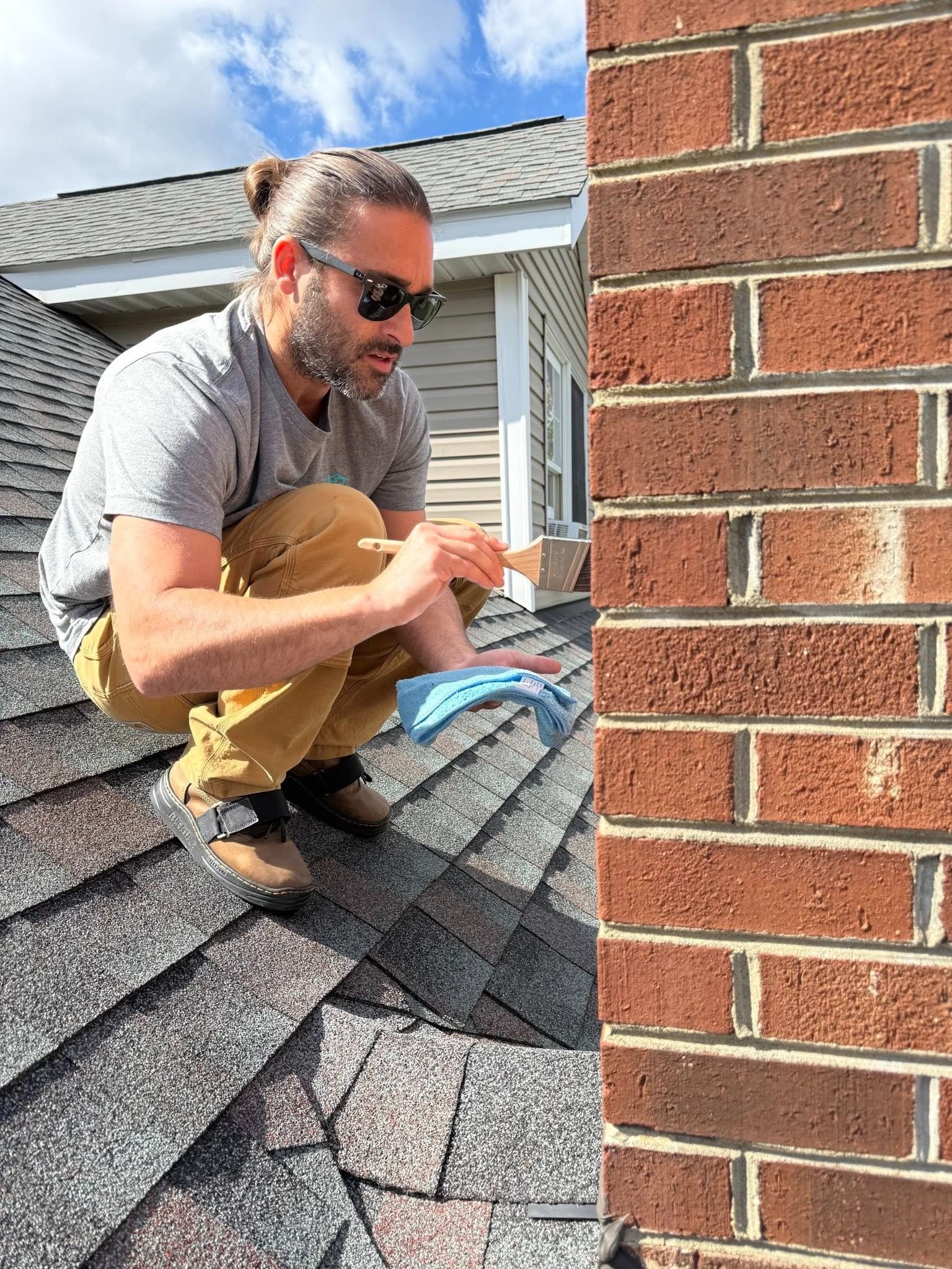 Man on a roof repairs chimney with a tool and a cloth; sunny day.