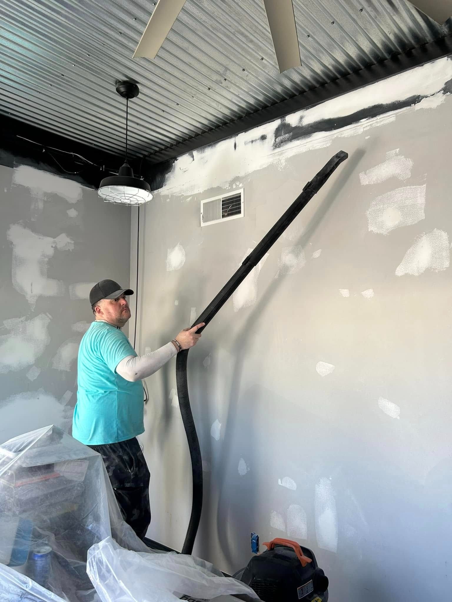 Person using a hose to work on a wall in a room; the wall is being prepped.