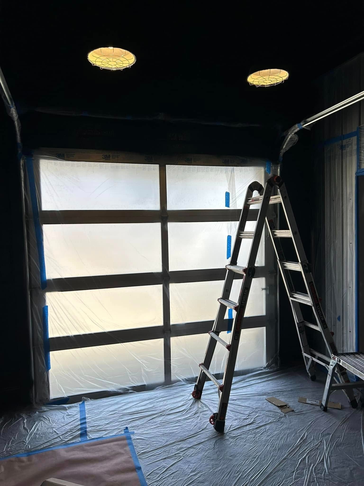 Interior shot of a room with a frosted glass garage door, a ladder, and overhead lights.