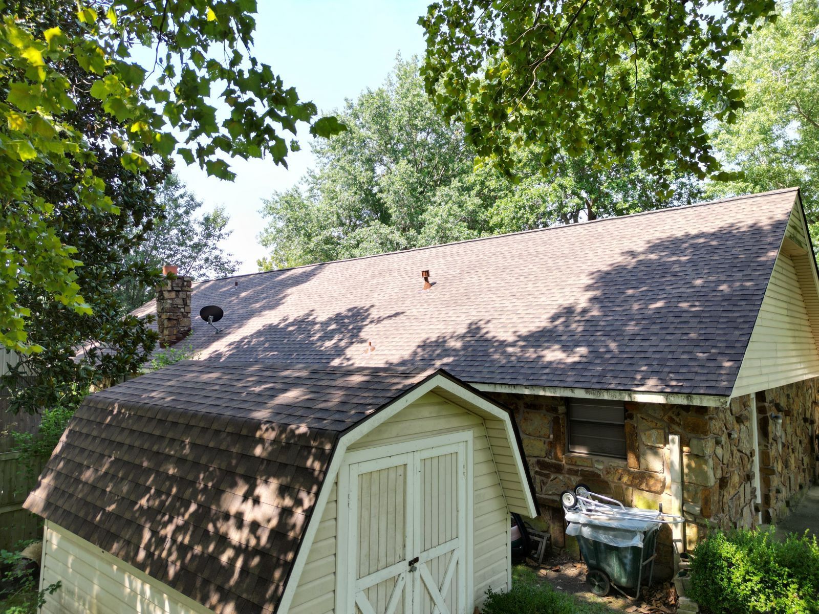 A garage with a roof that is covered in shingles is next to a house.