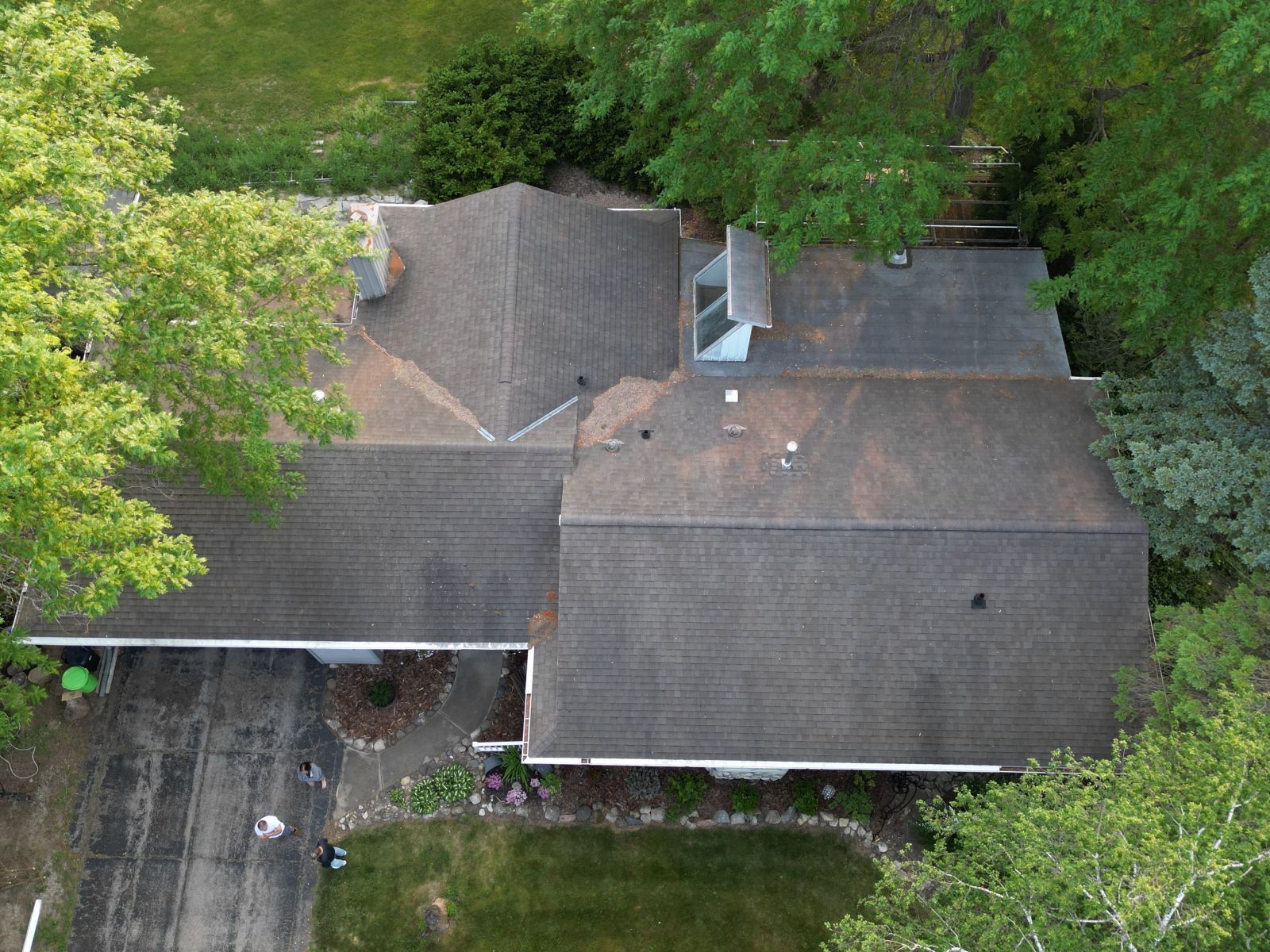 An aerial view of a house with a roof and a driveway surrounded by trees.