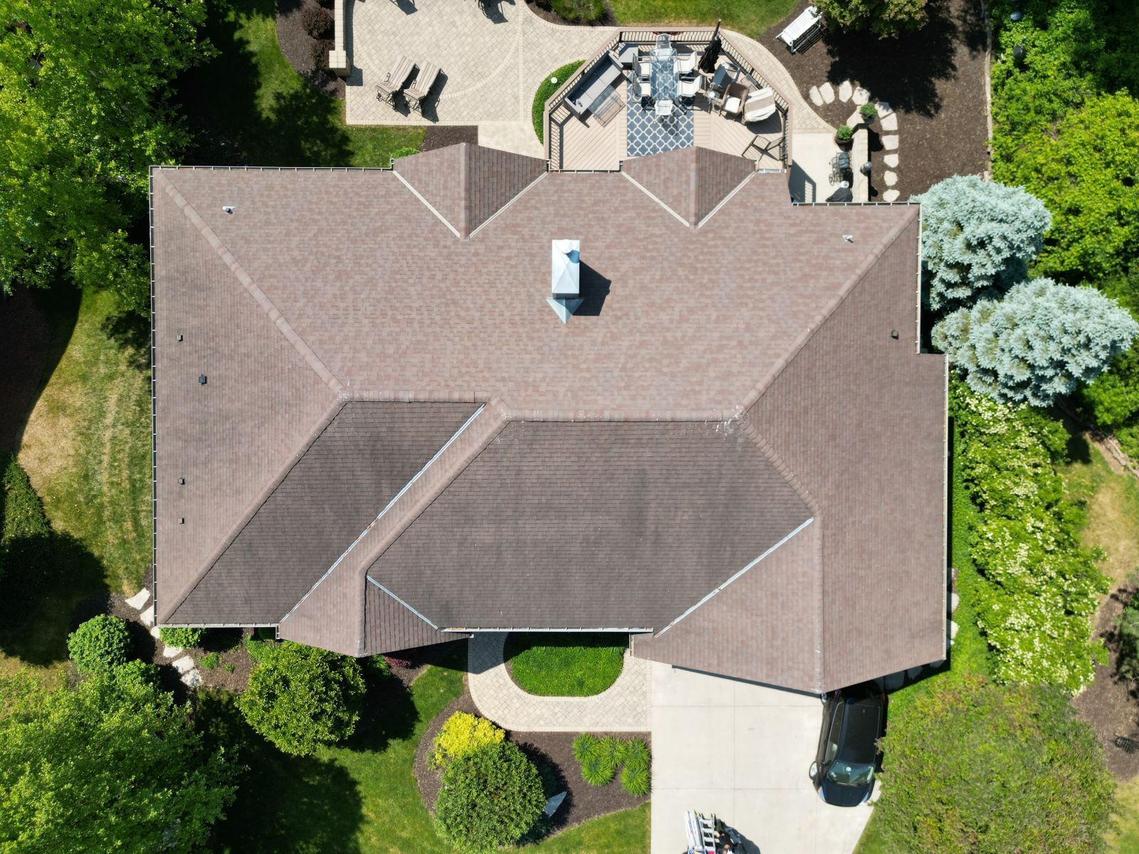 An aerial view of a large house with a roof and a driveway surrounded by trees.