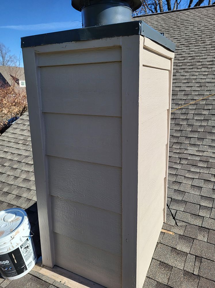 A chimney on top of a roof next to a bucket of paint.