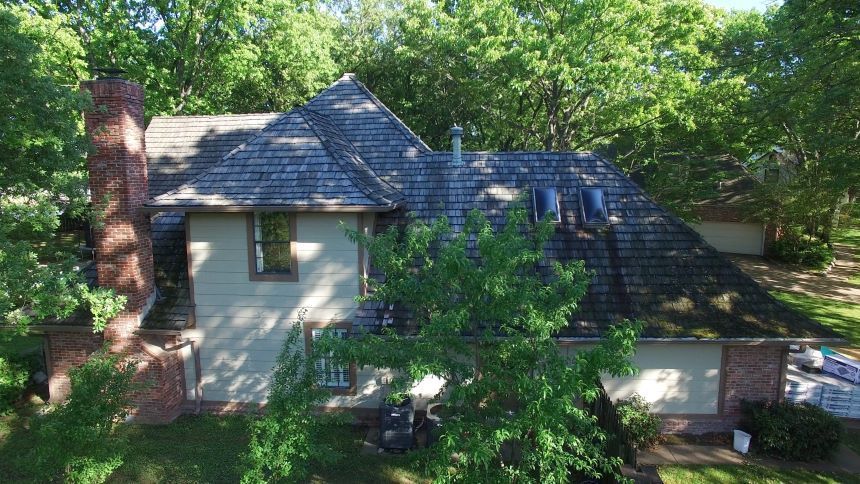 An aerial view of a large house with a slate roof surrounded by trees.