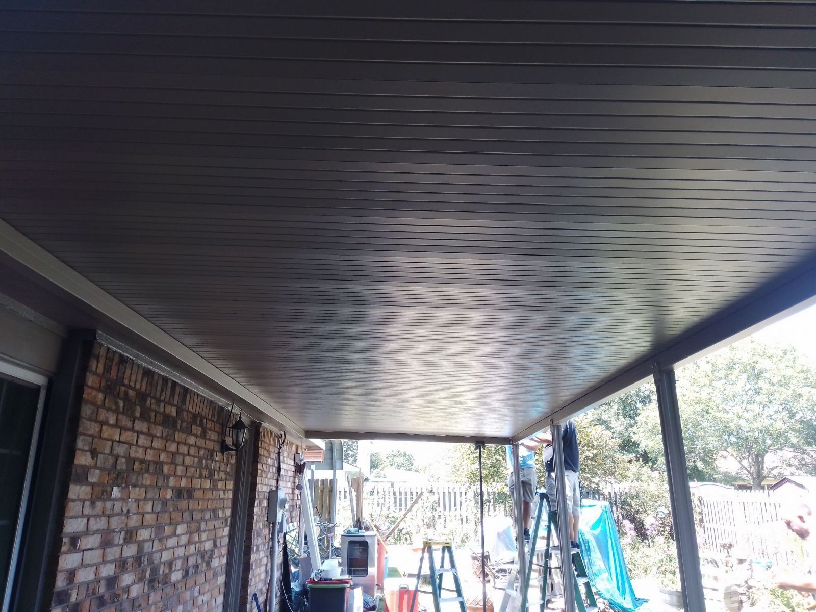 A ceiling of a porch with a brick wall and a ladder.