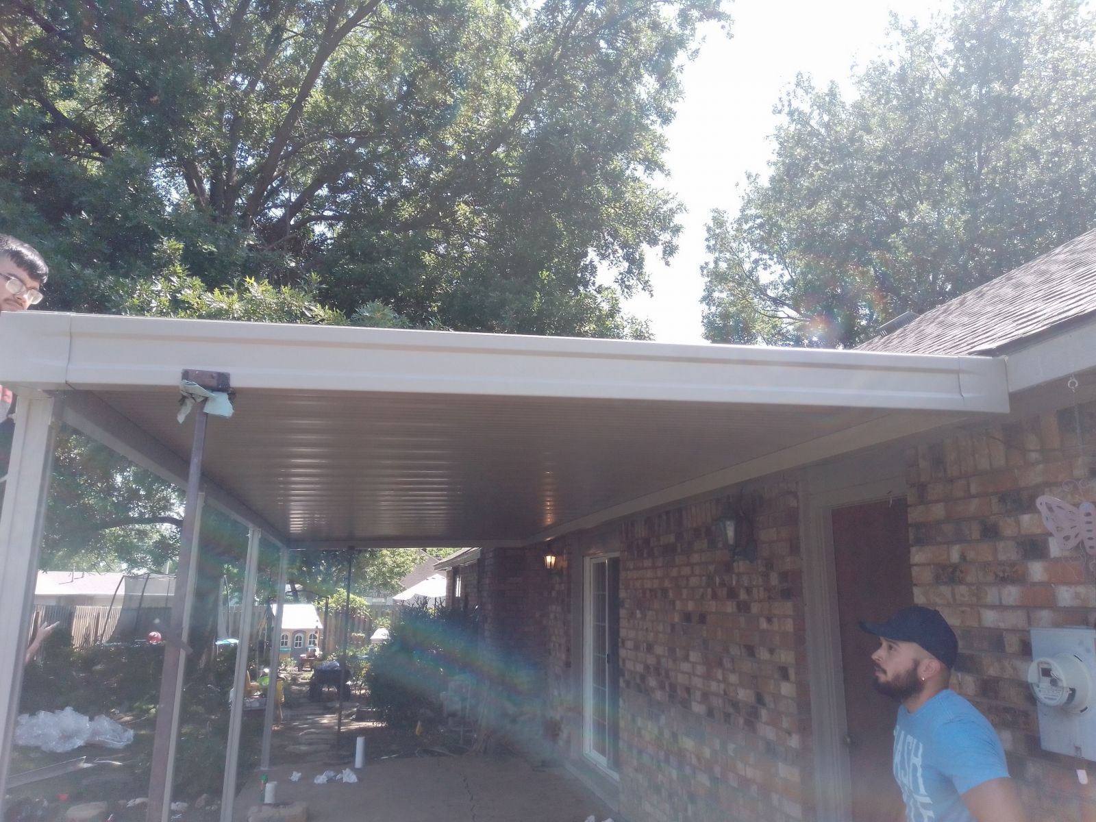 A man is standing under a covered patio in front of a brick house.