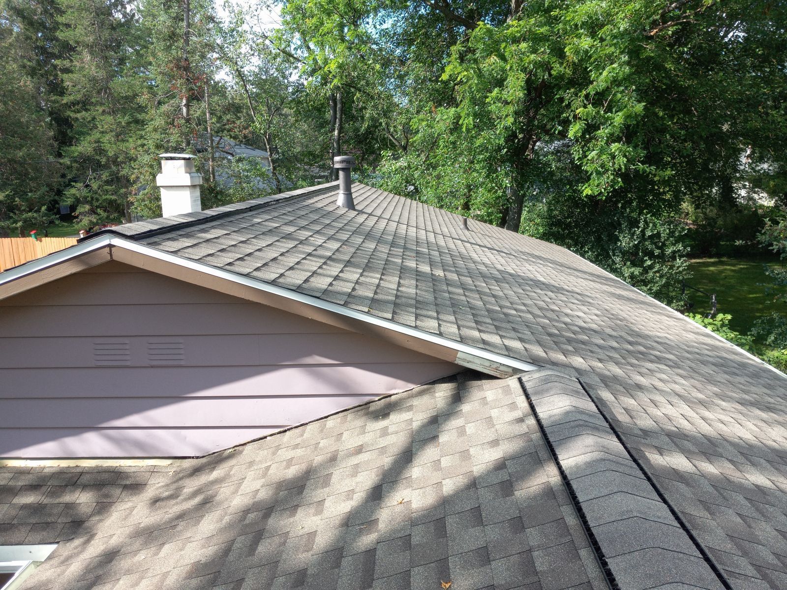 A roof of a house with a chimney and trees in the background.