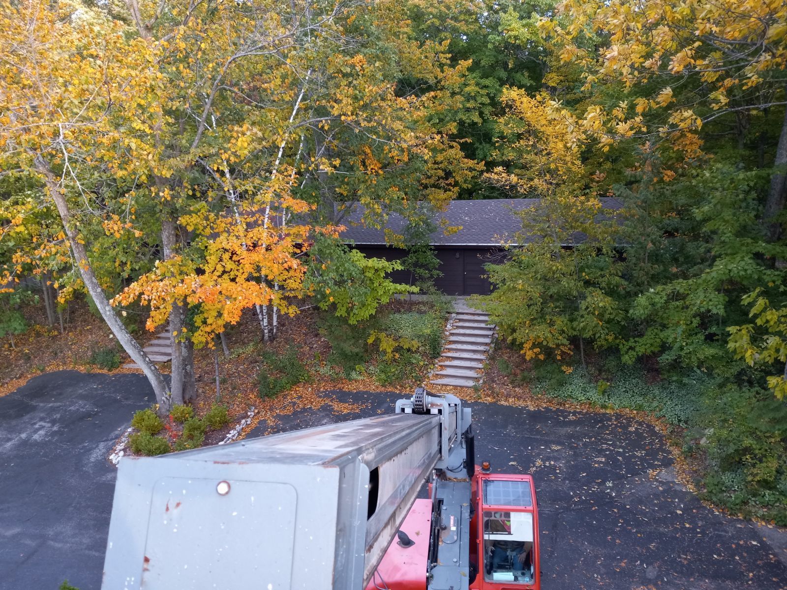 An aerial view of a crane in front of a house in the woods.