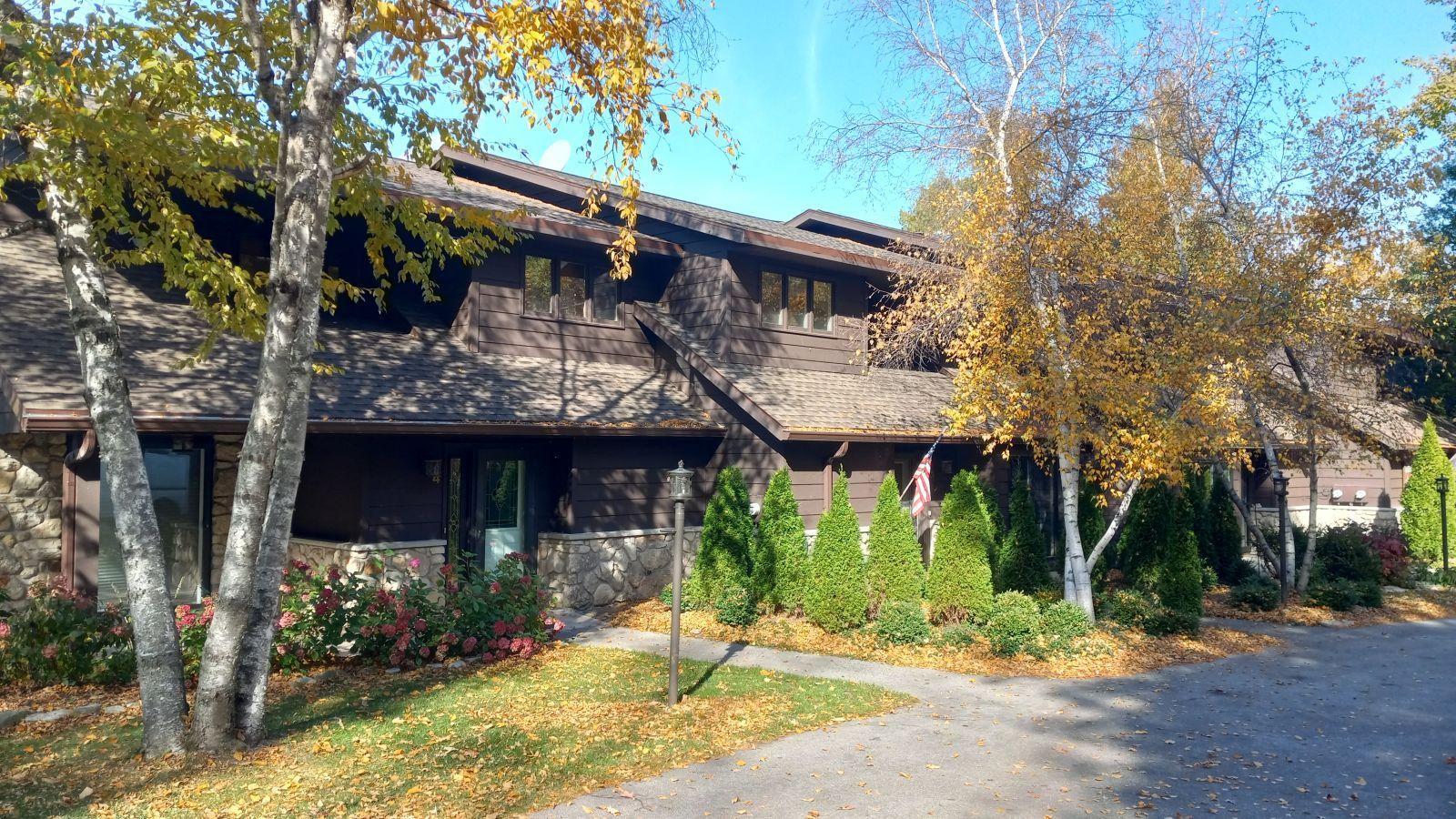 A large house is surrounded by trees and leaves on a sunny day.