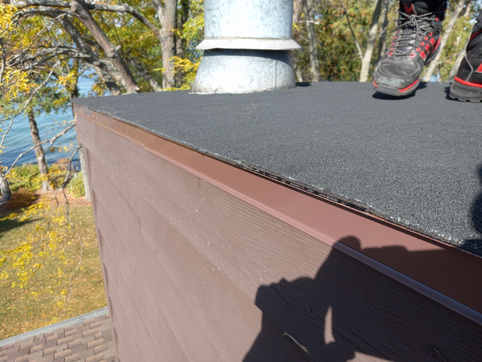 A person is standing on top of a roof next to a chimney.