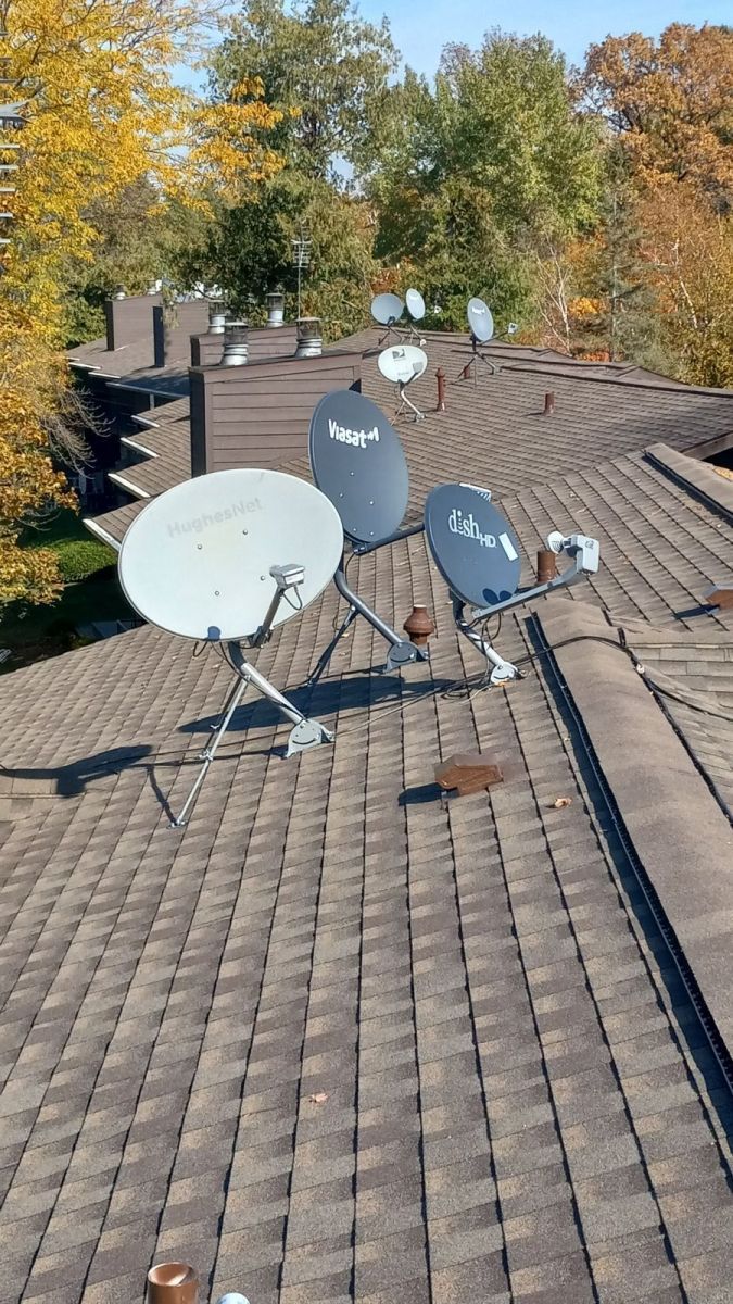 There are many satellite dishes on the roof of a house.
