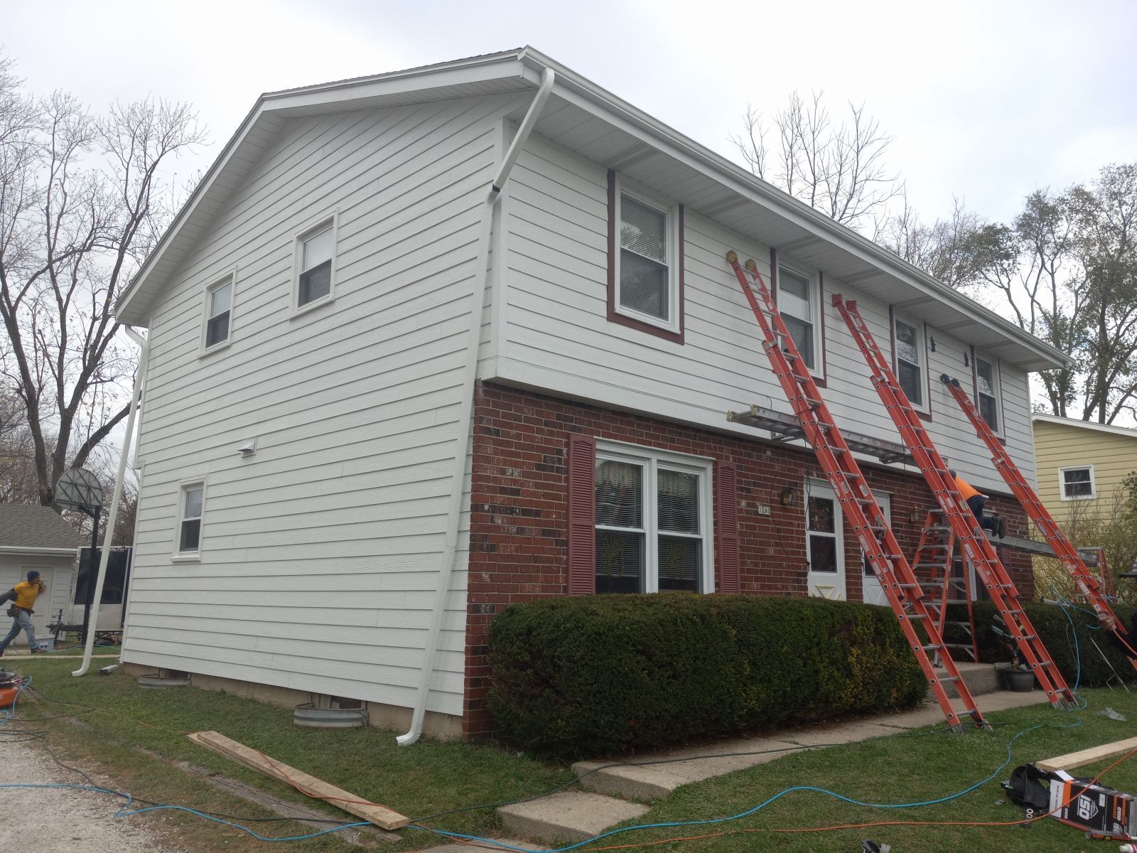 A house with a white siding and red ladders on the side of it.
