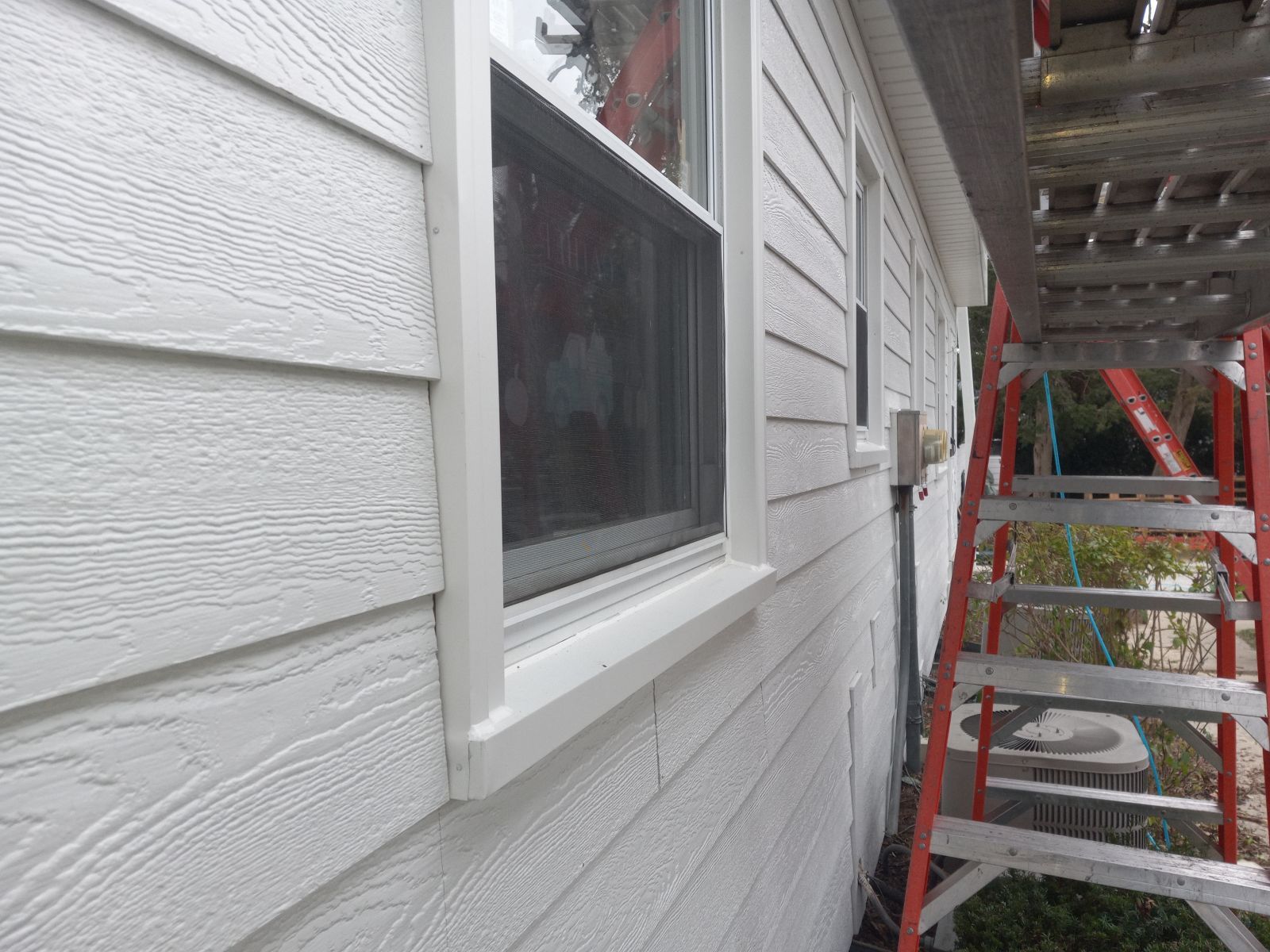 A white house with a window and a ladder on the side.