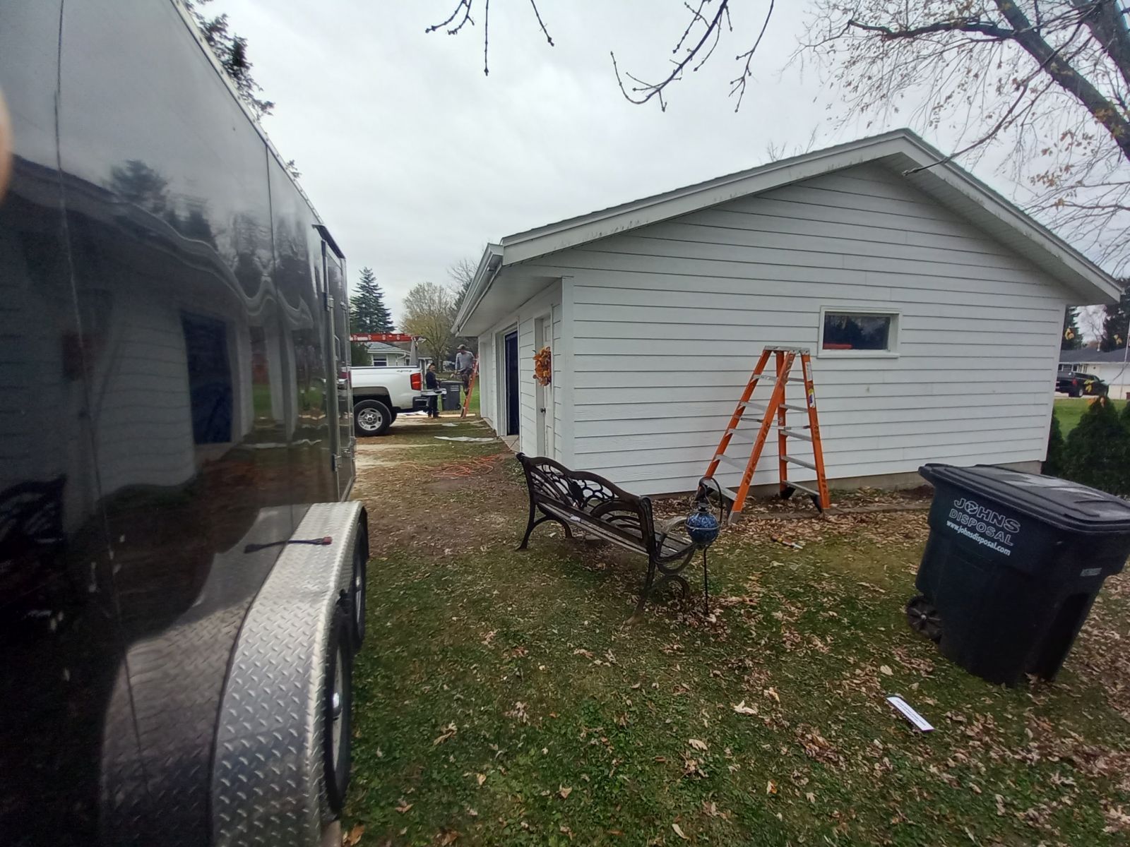 A black trailer is parked in front of a white house.