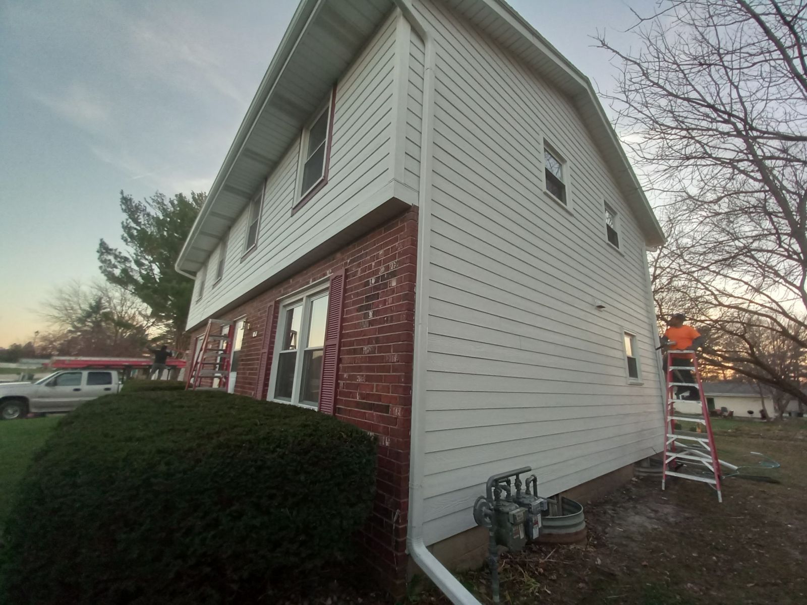 A man is standing on a ladder on the side of a house.