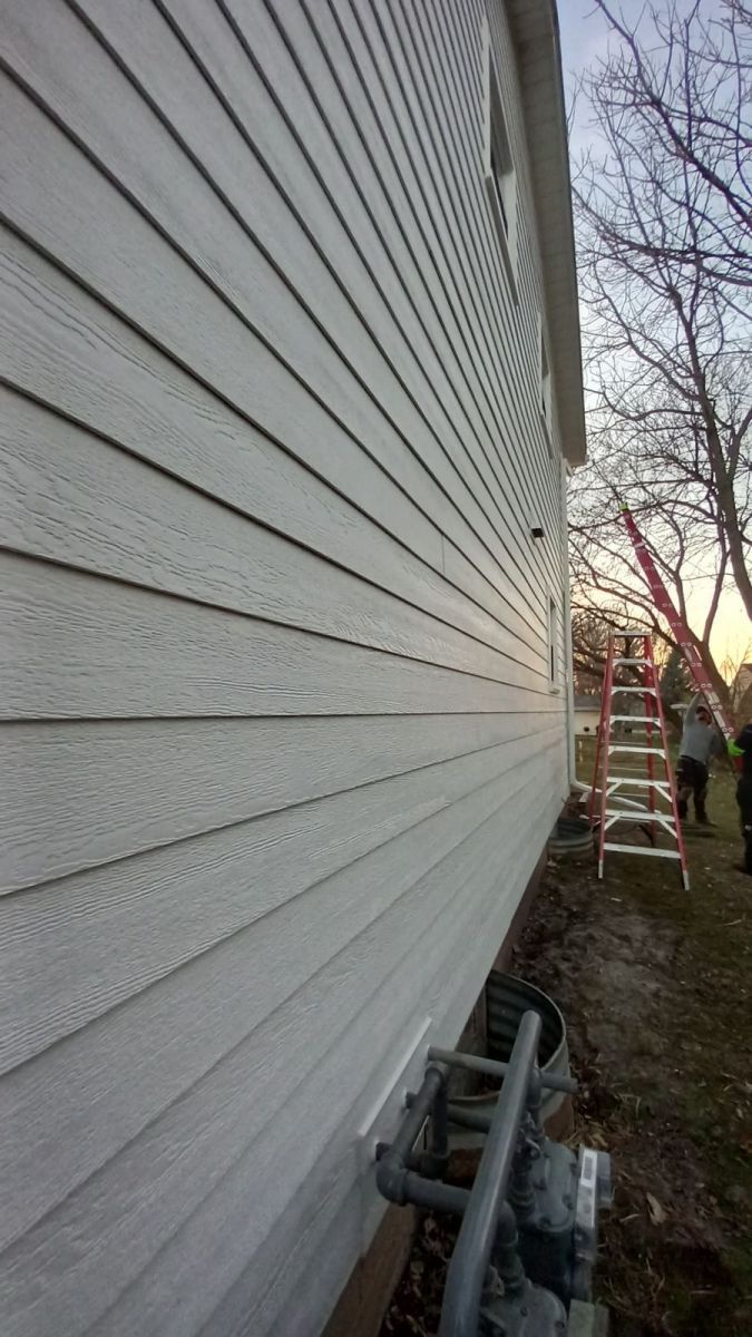 A man is standing on a ladder next to a white house.