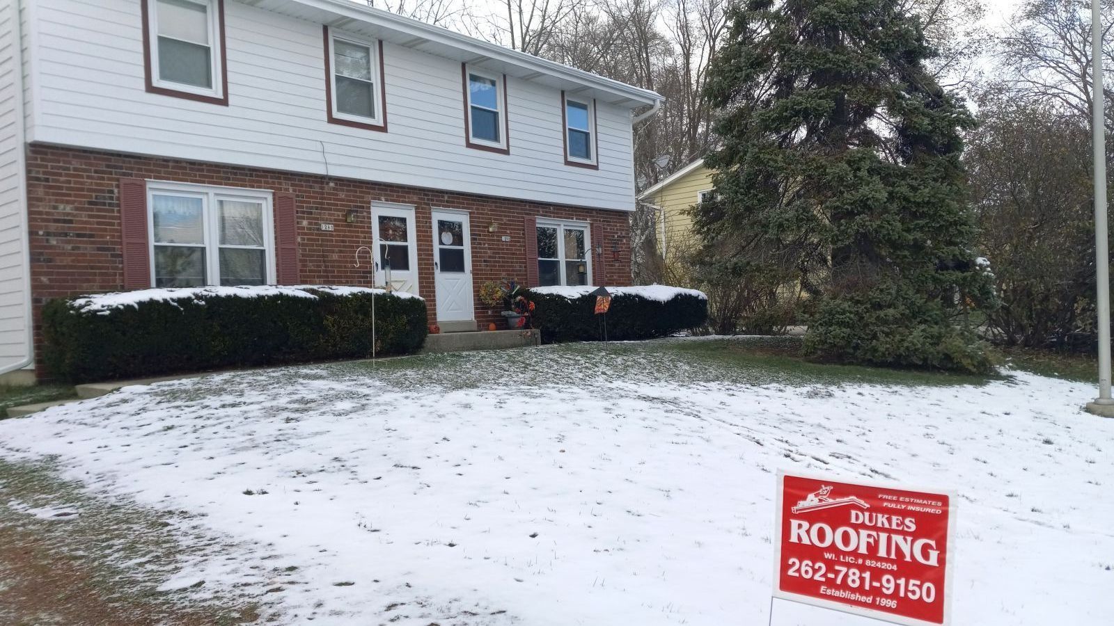 A house with a roofing sign in front of it.