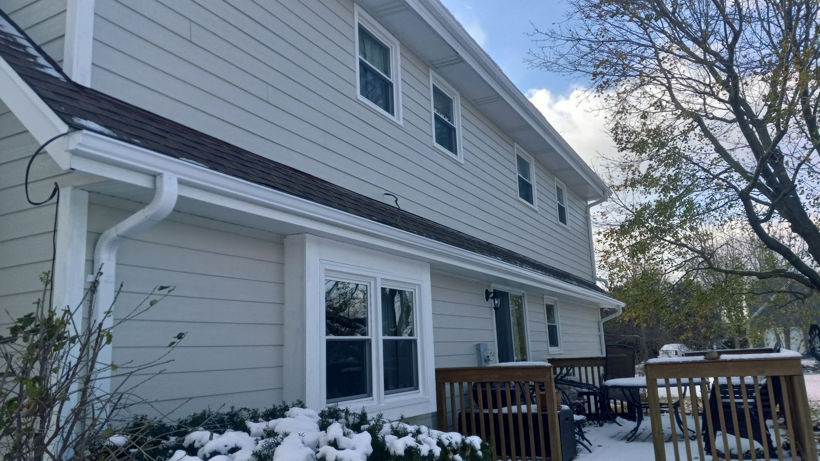 A large white house with a deck and snow on the ground.