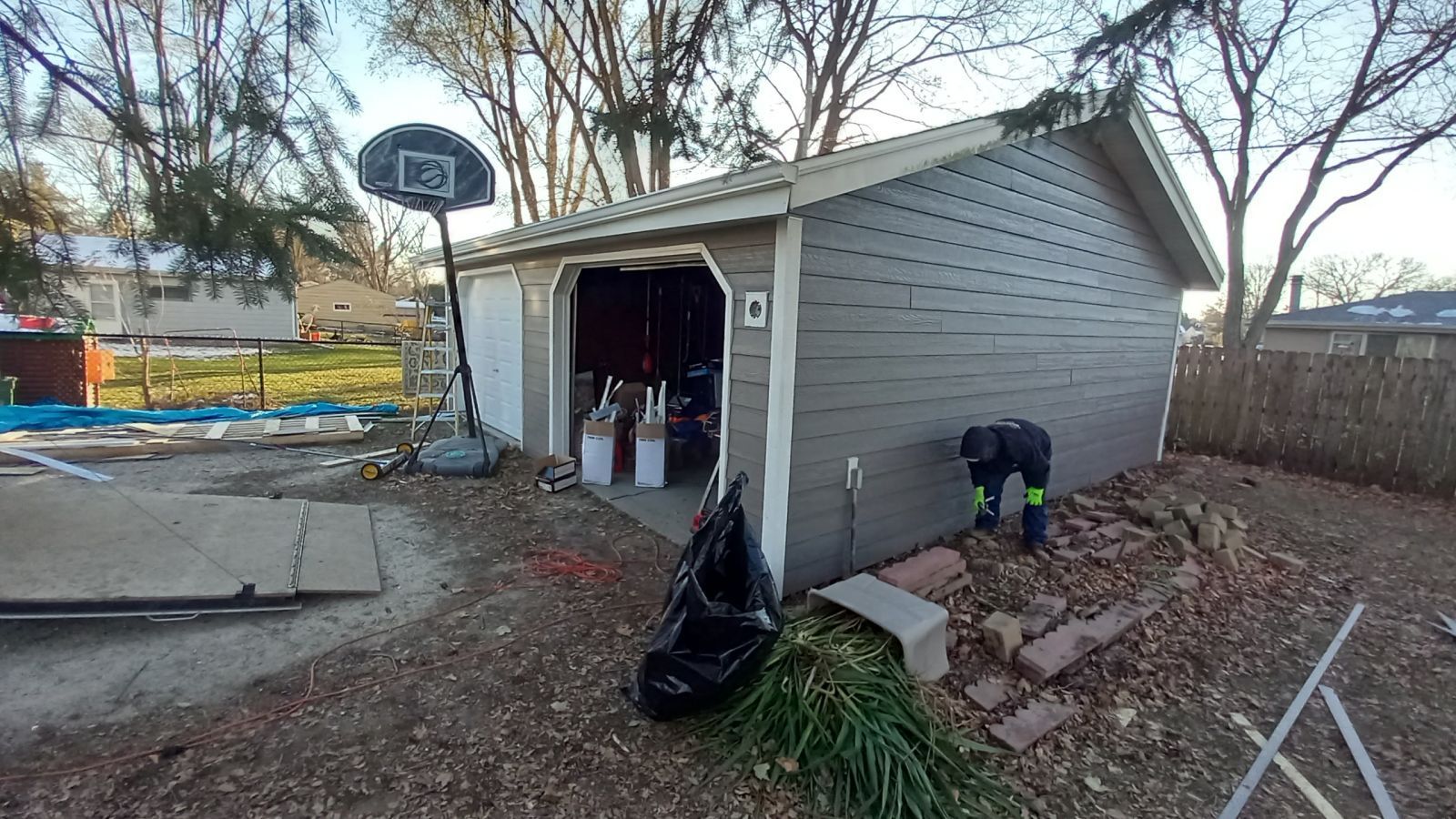A man is standing in front of a garage with a basketball hoop in the background.