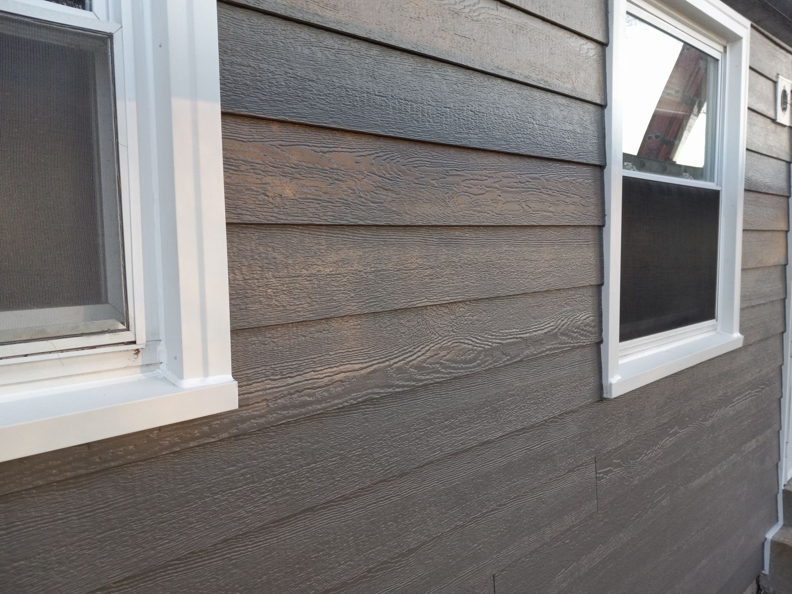 A close up of a house with gray siding and white windows.