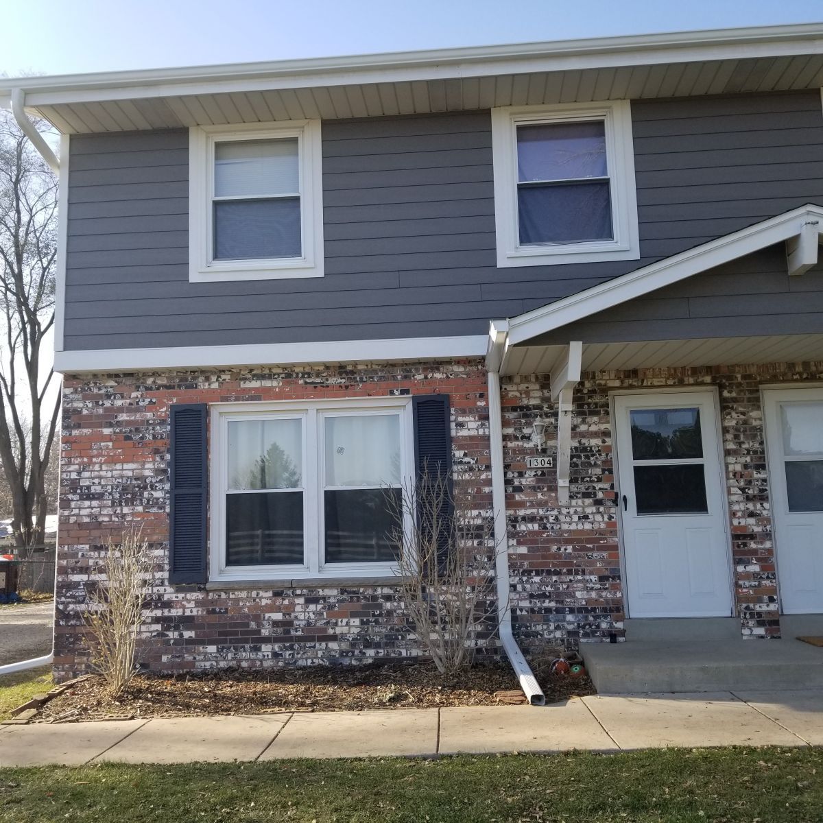 A brick house with a gray siding and white doors