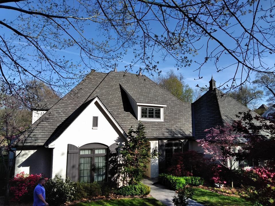 A man stands in front of a white house with a gray roof
