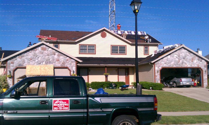 A green truck is parked in front of a house under construction