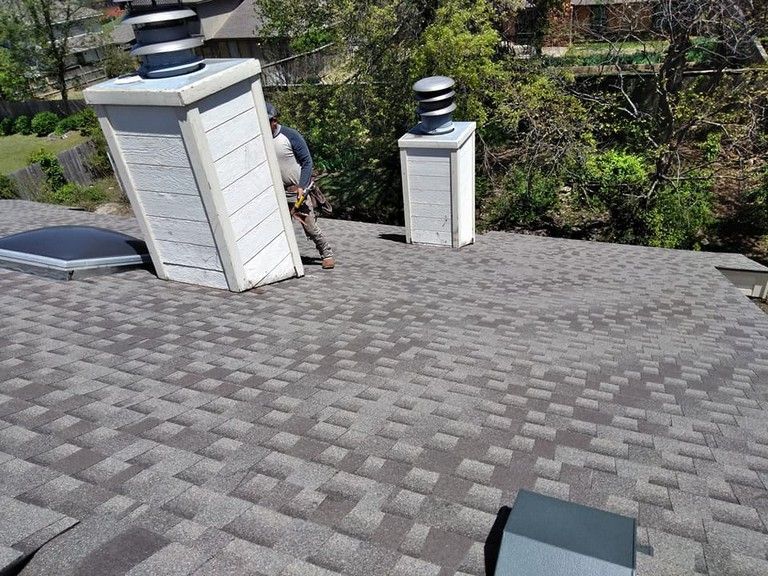 A man is standing on top of a roof with chimneys.