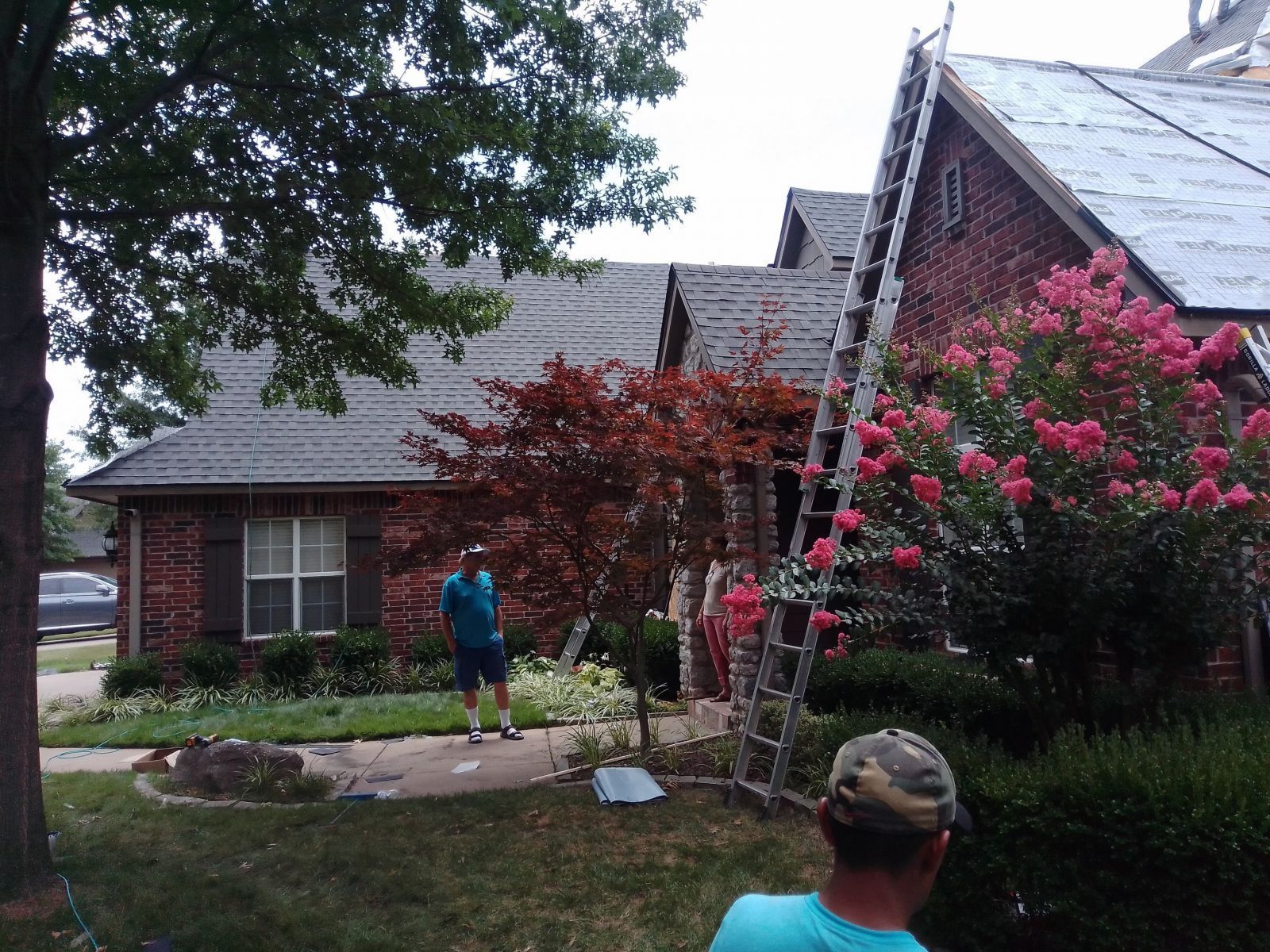 A man in a blue shirt is standing in front of a house