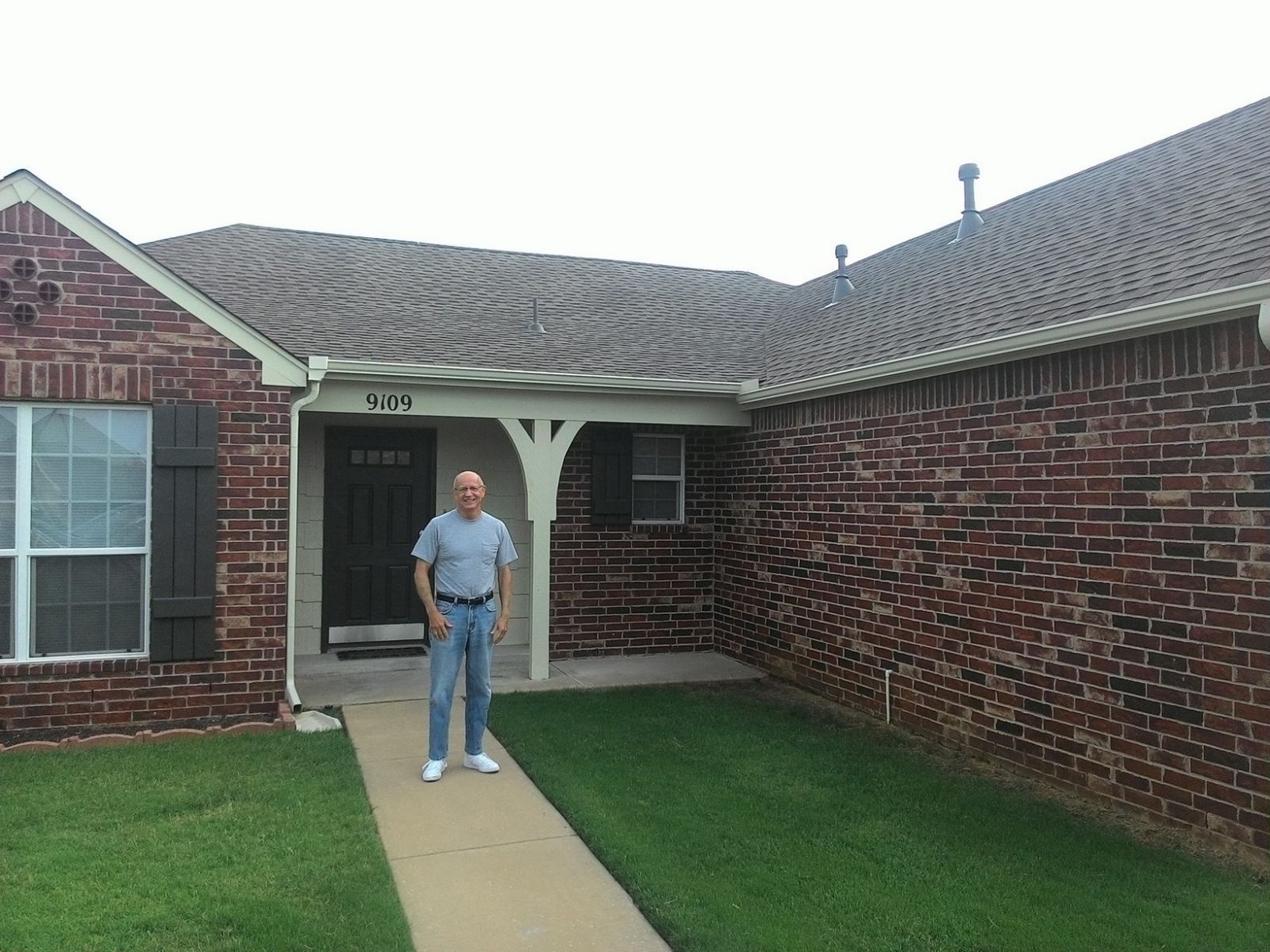 A man is standing in front of a brick house.