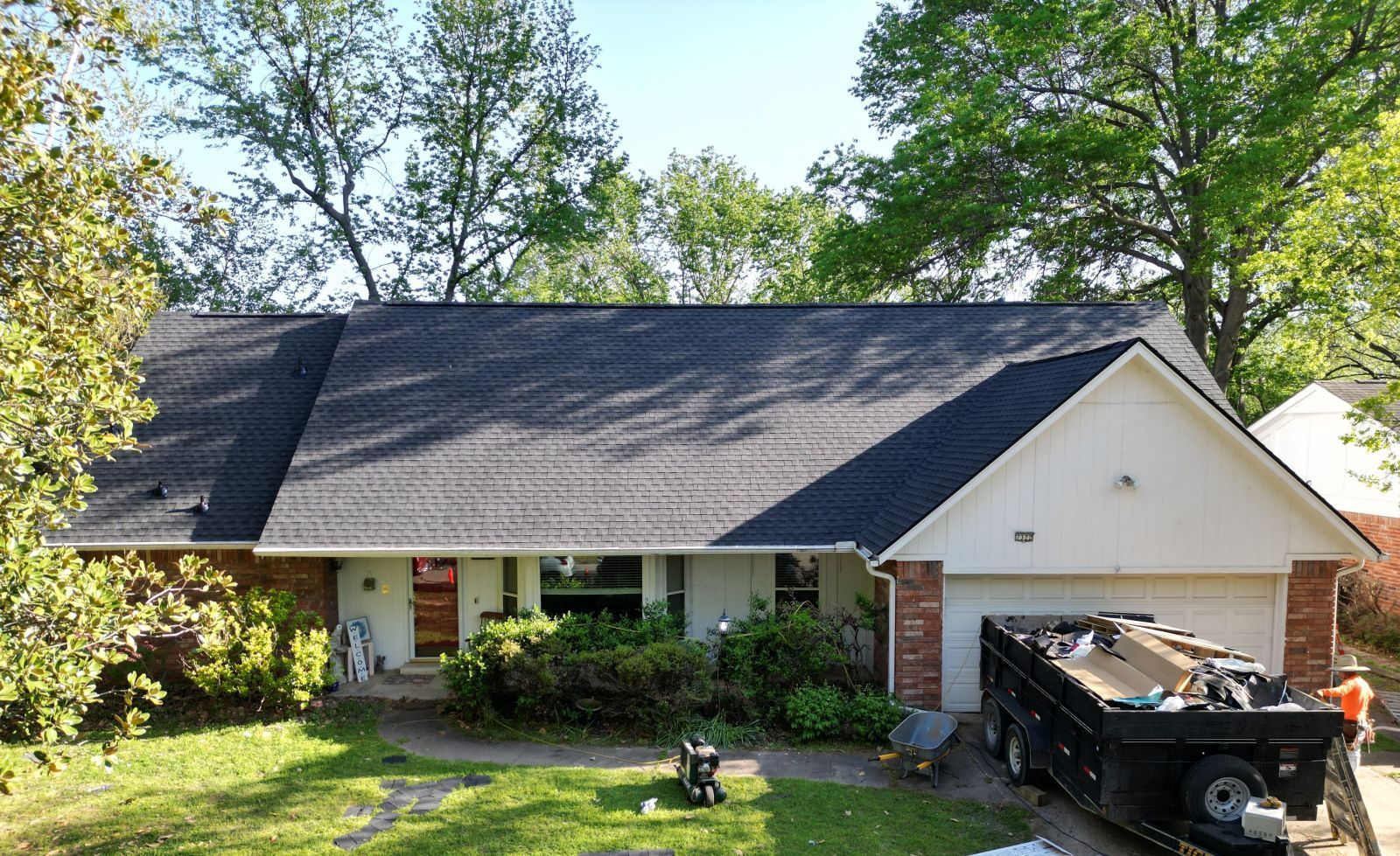 A house with a black roof and a dumpster in front of it.