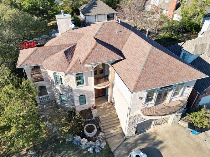 An aerial view of a large house with a brown roof surrounded by trees.