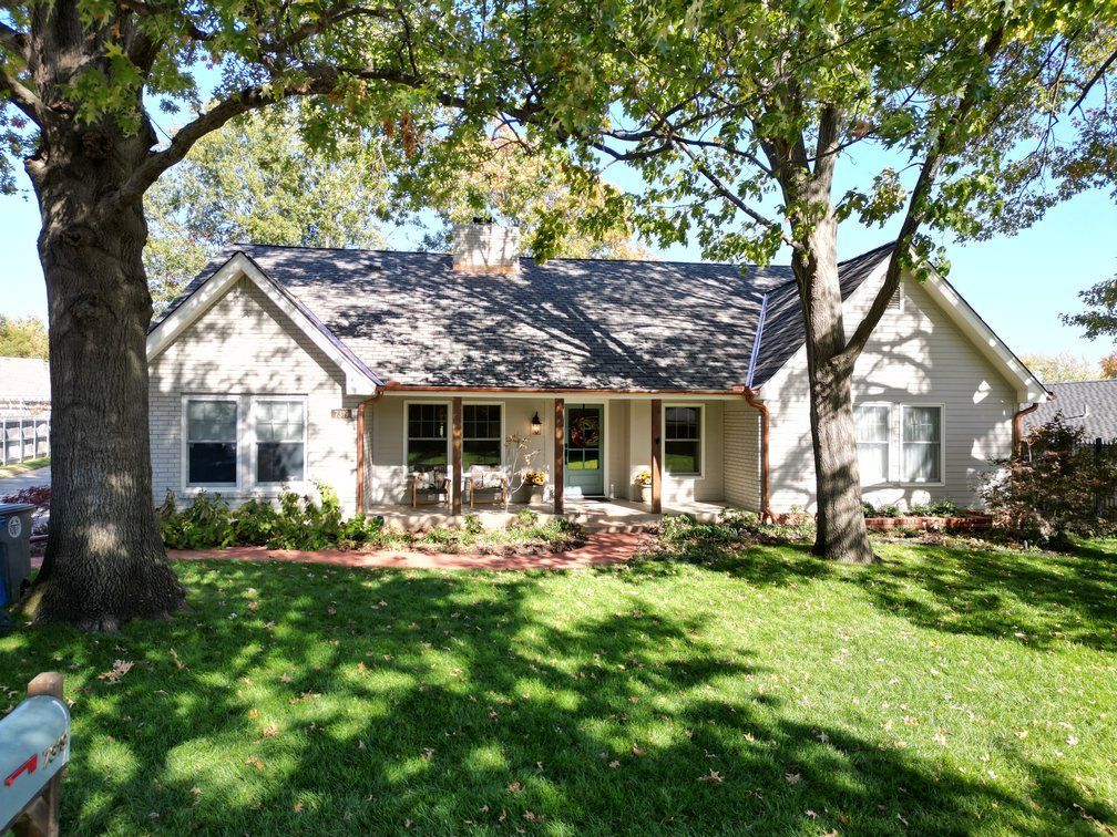 A white house with a gray roof is sitting on top of a lush green lawn.