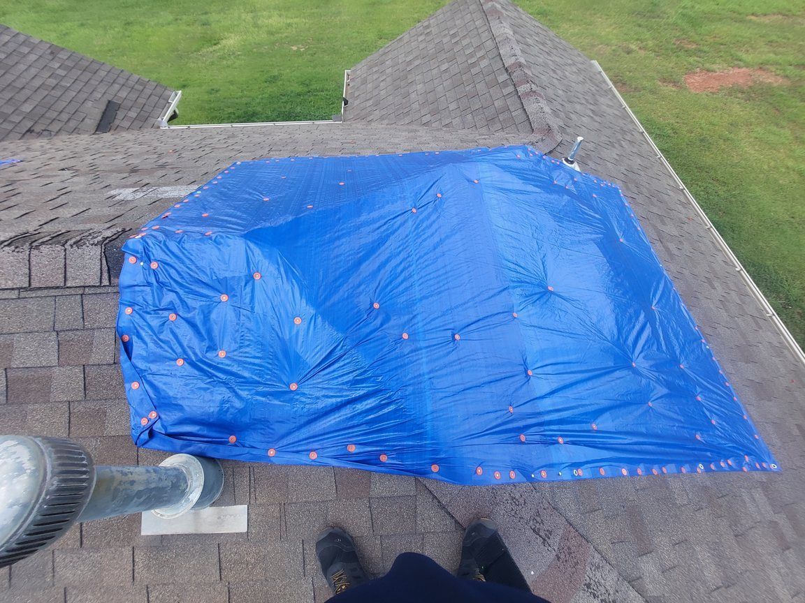 A blue tarp is covering a hole in the roof of a house.