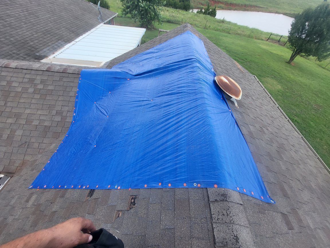 A person is holding a blue tarp on top of a roof.